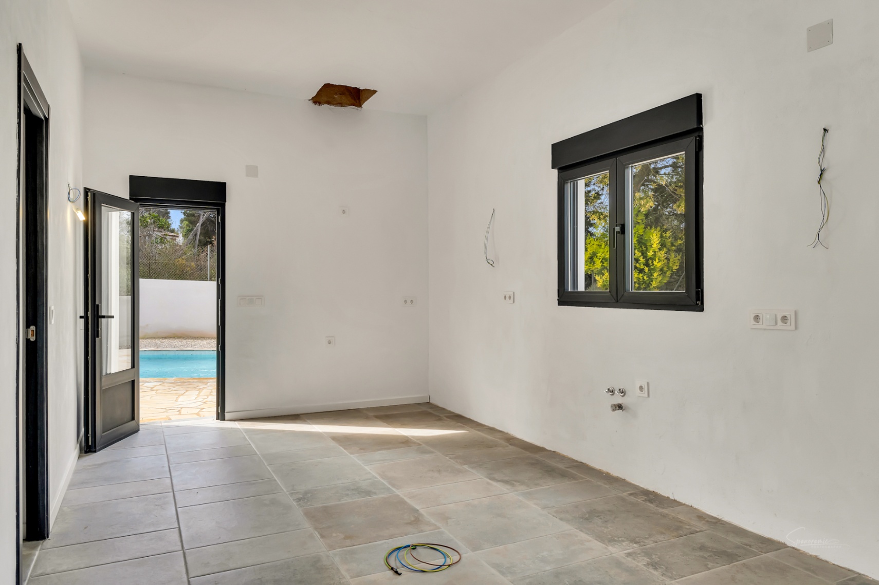Habitación en proceso de reforma con suelos de piedra natural, carpintería negra y acceso directo a la zona exterior con piscina y terraza.