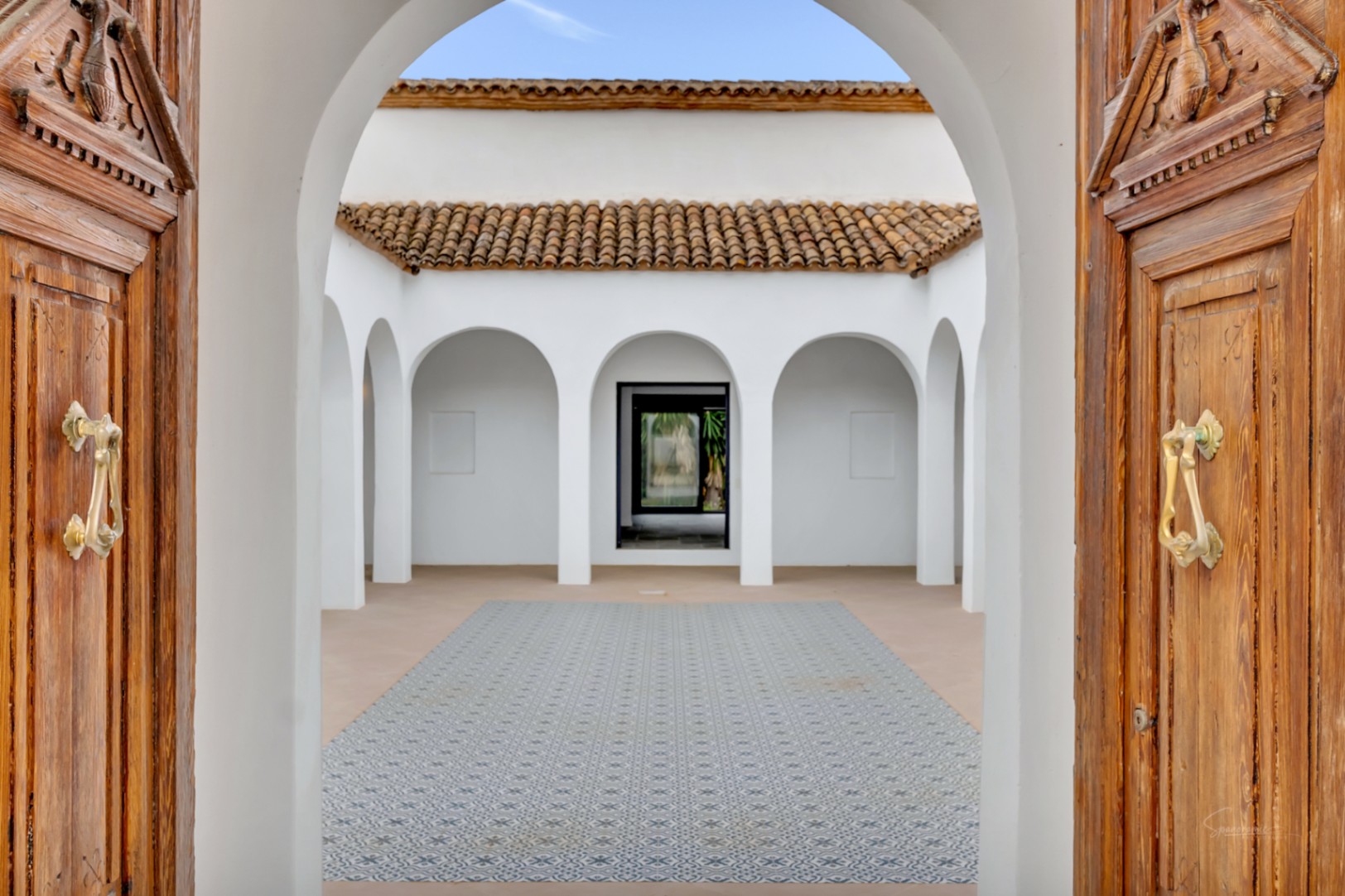Patio interior central con arcos de medio punto, suelos de baldosa hidráulica decorativa y puertas de madera tallada con herrajes de latón.