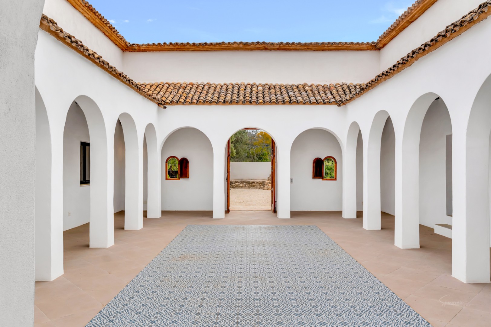 Patio interior central con arcos de medio punto, suelos de baldosas estampadas y cubiertas de teja de terracota que rodean el espacio abierto.