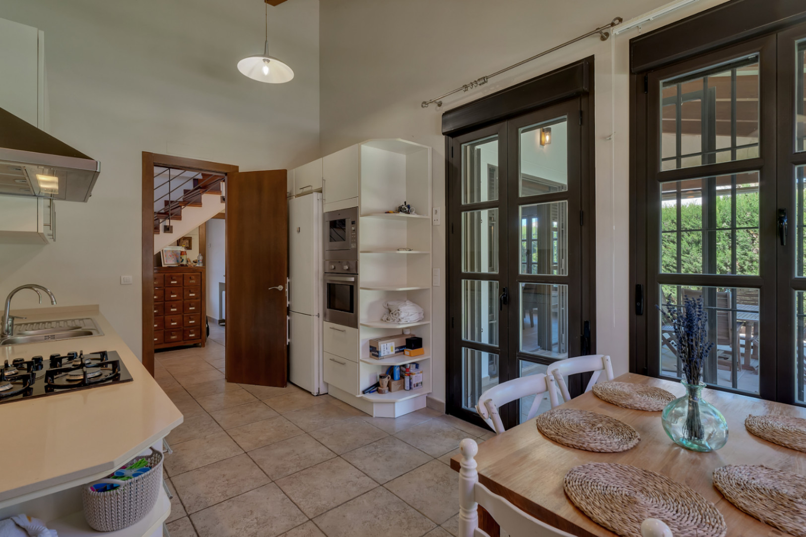 Cocina equipada con armarios blancos, encimera clara y zona de comedor. Incluye techos altos, suelos cerámicos y acceso directo a la terraza a través de amplios ventanales.