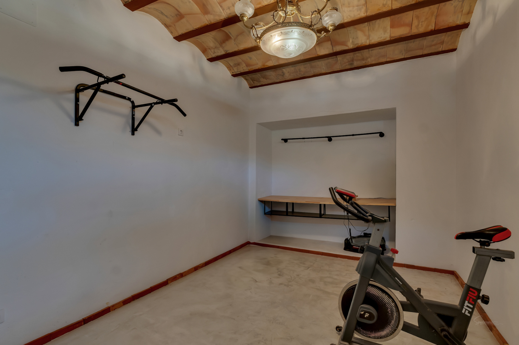 Sala polivalente o gimnasio con techos de bovedilla cerámica y vigas de madera. Incluye bicicleta estática, barra de dominadas y zona de trabajo integrada.