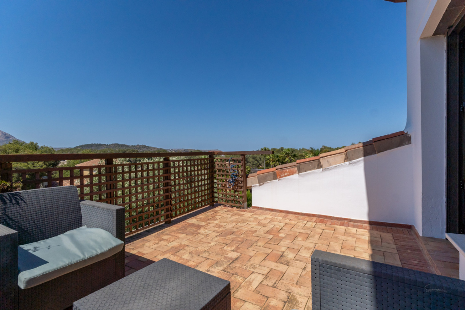 Terraza privada en la planta superior con suelo de barro cocido, mobiliario de ratán sintético y barandilla de madera con vistas despejadas al entorno natural.
