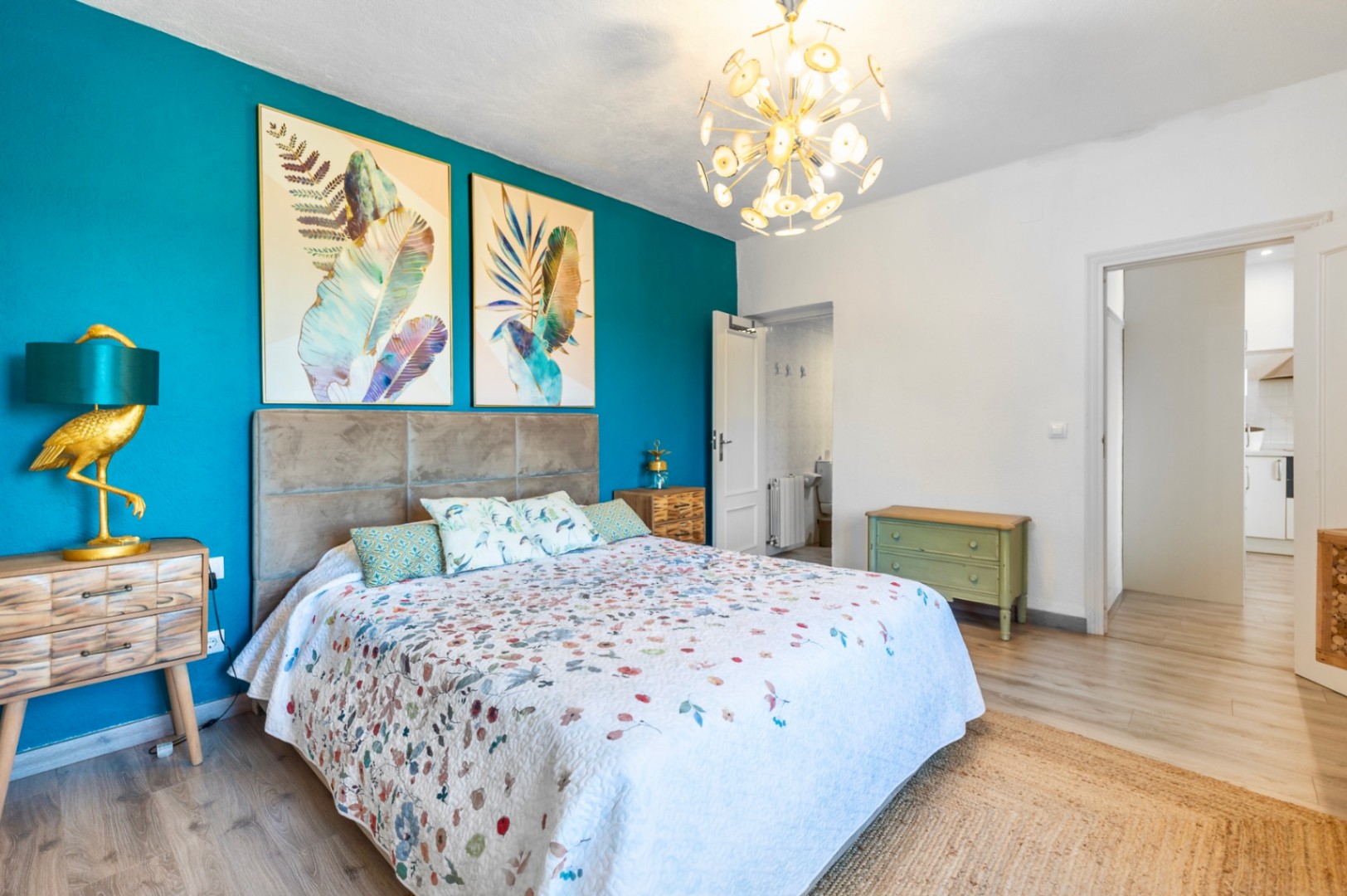 Dormitorio con pared de acento turquesa, cabecero tapizado gris y lámpara de diseño. Dispone de baño en suite, suelos de madera y acceso directo a las estancias comunes.