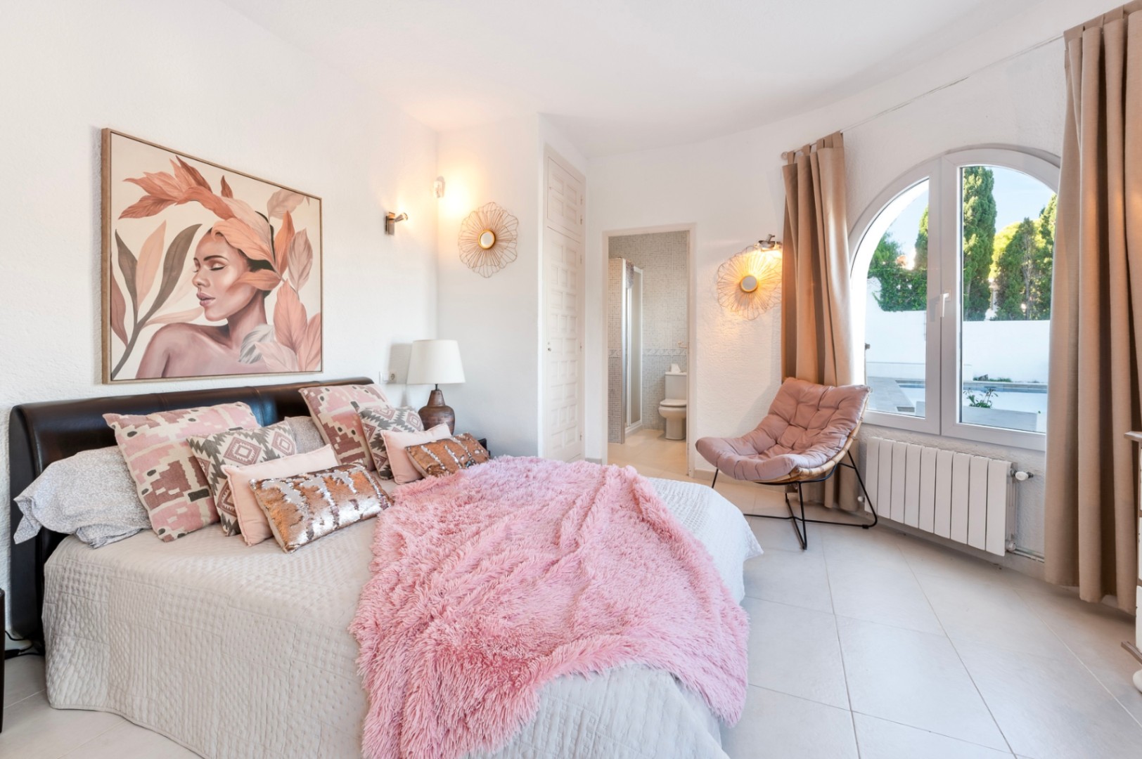 Dormitorio principal con baño en suite, ventanal de arco con vistas al exterior y decoración en tonos cálidos. Incluye suelos cerámicos y calefacción por radiador.