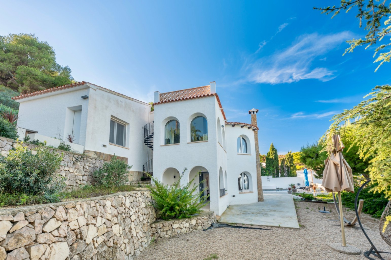 Fachada blanca de estilo mediterráneo con arcos tradicionales, escalera de caracol exterior y muros de piedra seca integrados en el entorno natural de Portitxol.