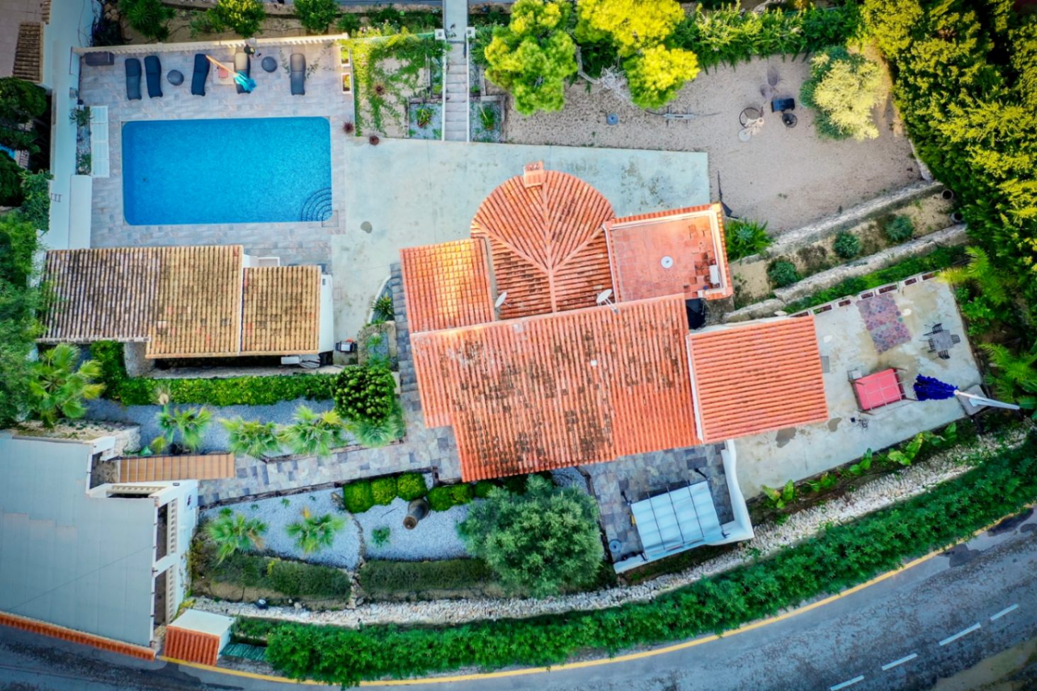 Vista aérea cenital de la propiedad que muestra la distribución de la parcela, la piscina rectangular, los techos de teja y los jardines con palmeras y senderos de piedra.