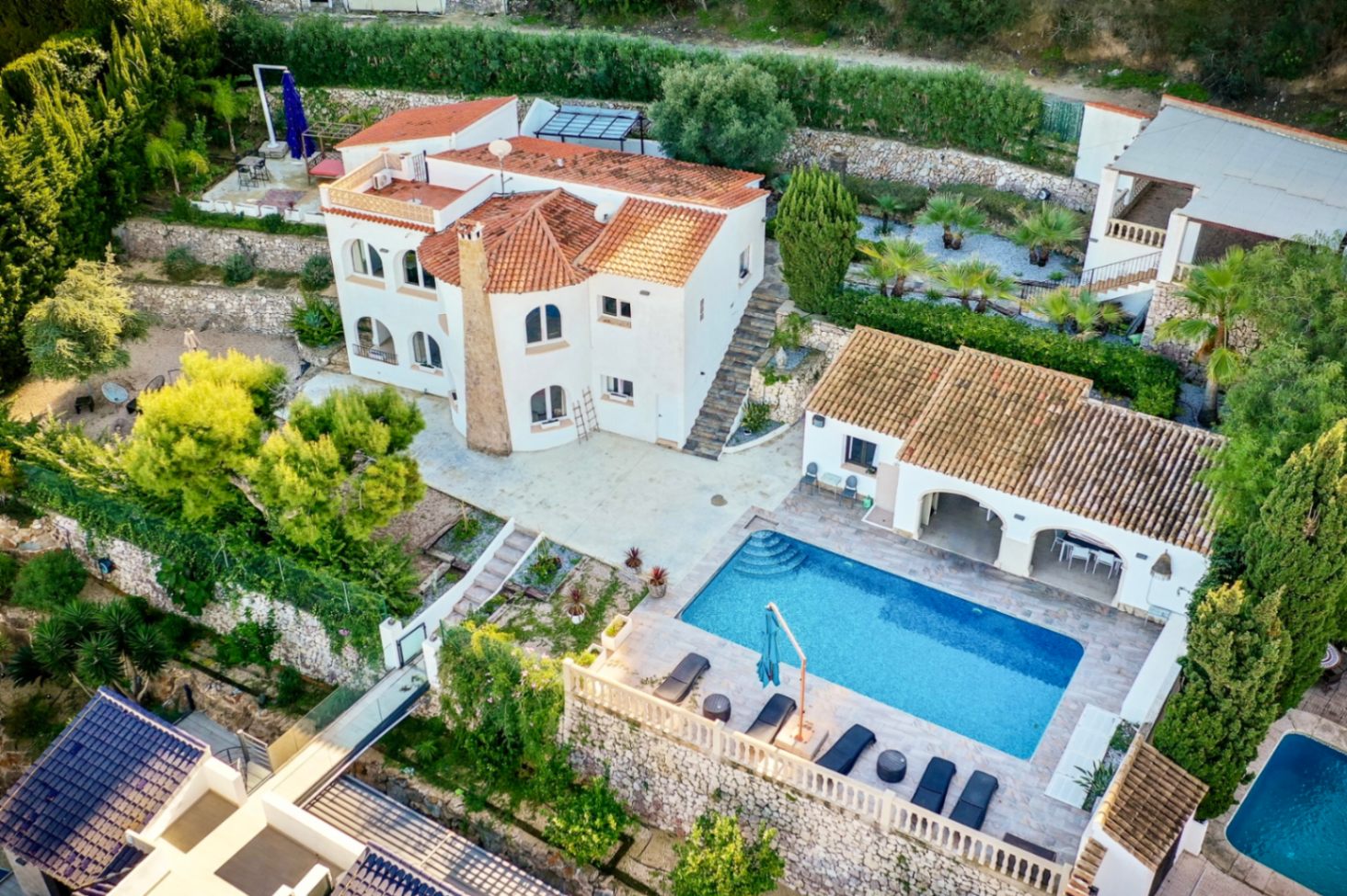 Vista aérea de la villa con arquitectura mediterránea, destacando la piscina rectangular, amplias terrazas de piedra y jardines escalonados en una parcela privada.