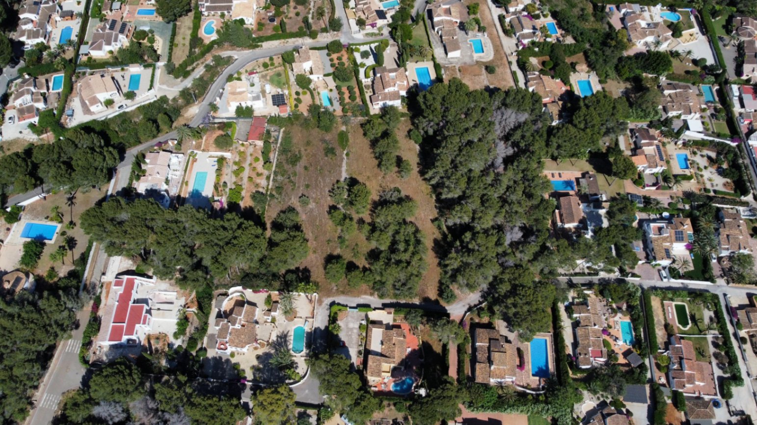 Vista aérea de la amplia parcela llana rodeada de chalets consolidados, destacando su arbolado autóctono y su ubicación privilegiada en una zona residencial tranquila.