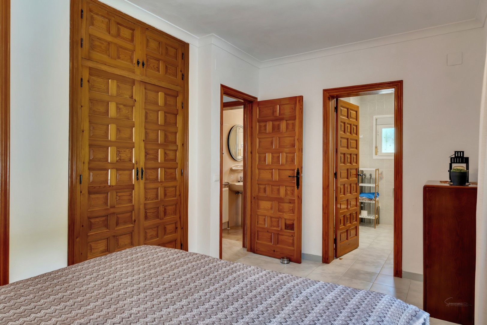 Dormitorio con amplios armarios empotrados de madera tallada y acceso directo a dos baños en suite, destacando la carpintería tradicional y suelos cerámicos.