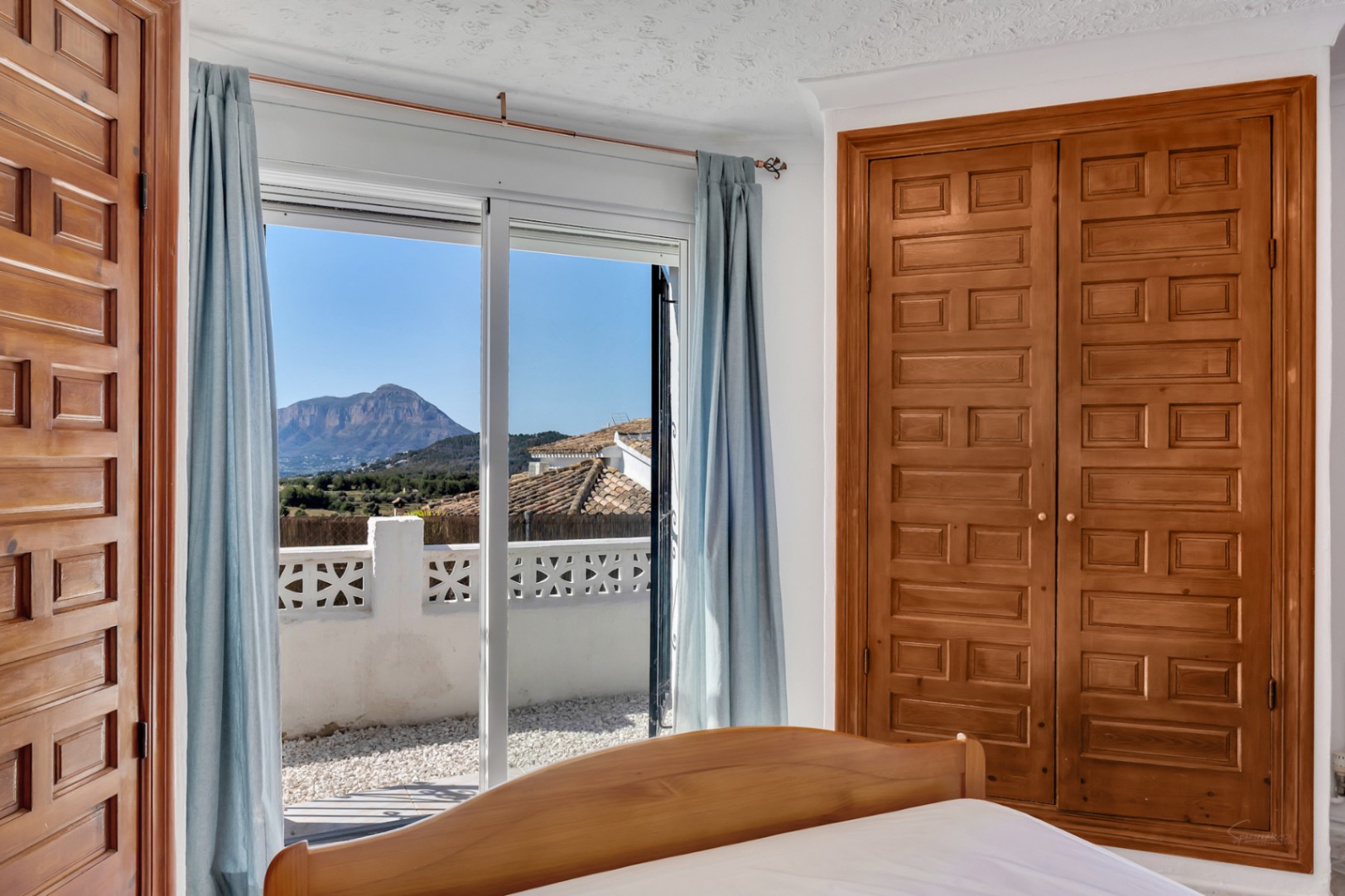 Dormitorio con armario empotrado de madera tallada y acceso directo a terraza con vistas despejadas al Montgó y luz natural abundante.