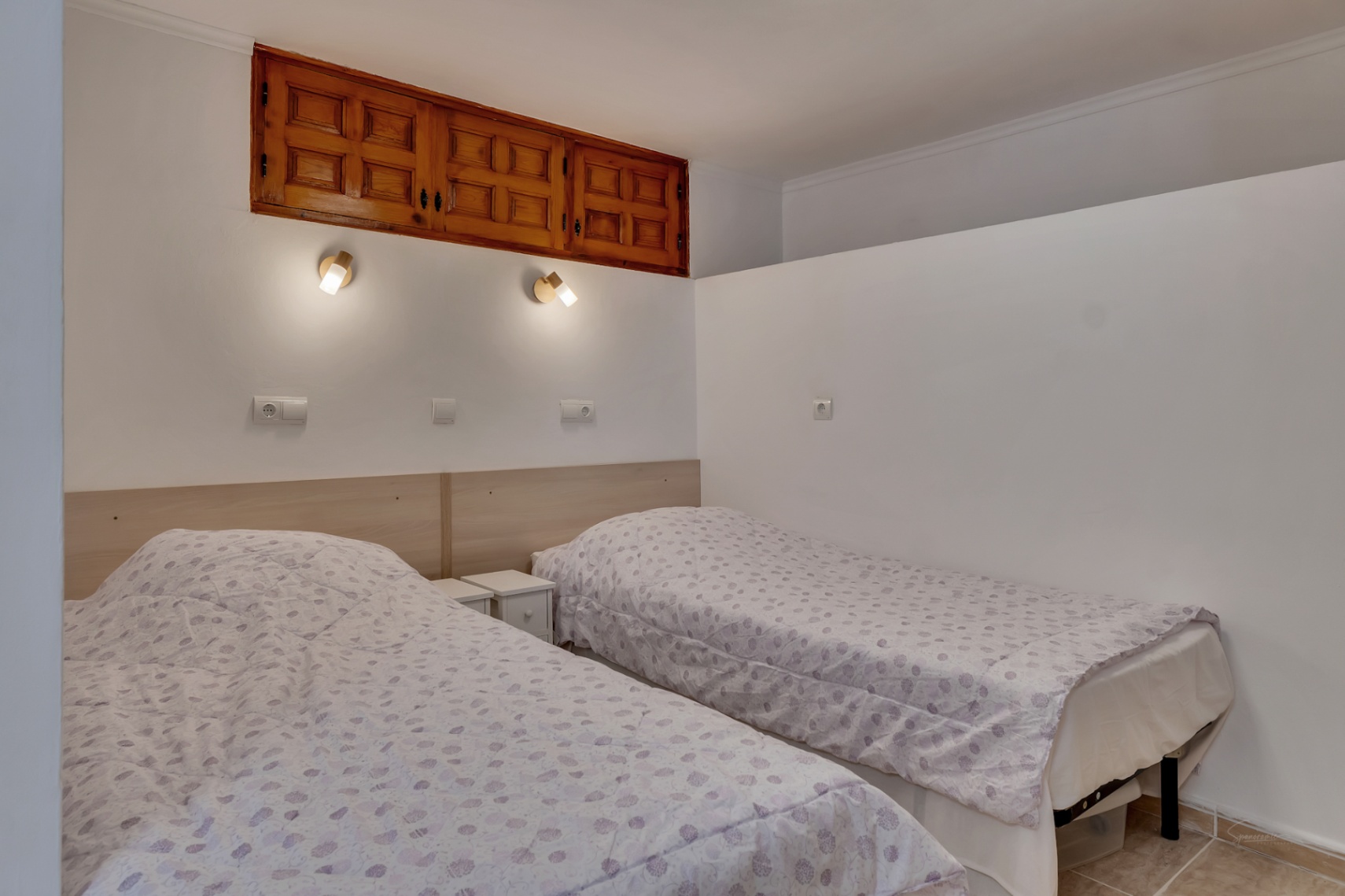 Dormitorio con dos camas individuales, cabecero de madera clara y armarios empotrados de estilo tradicional con cuarterones integrados en la pared blanca.