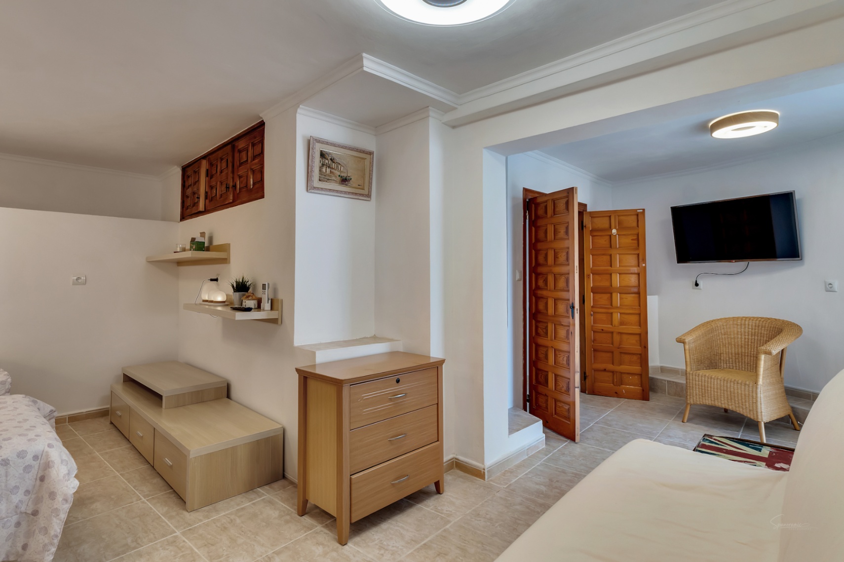 Dormitorio en planta inferior con suelos cerámicos, puertas de madera de estilo castellano, zona de estar con televisor y mobiliario funcional integrado.