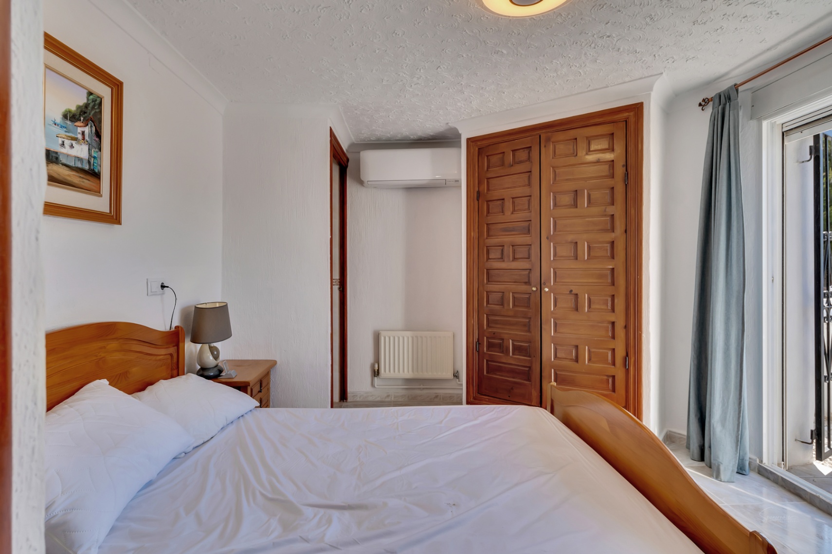 Dormitorio luminoso con cama de madera, armario empotrado de estilo rústico, aire acondicionado y acceso directo a la terraza exterior a través de puertas correderas.