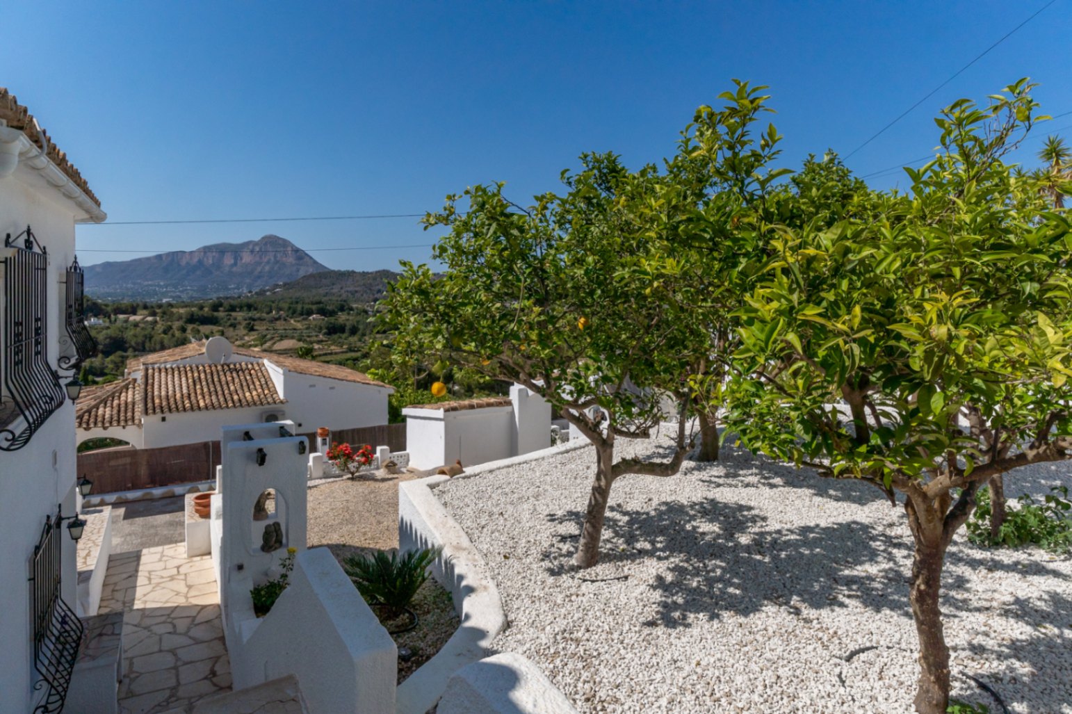 Jardín mediterráneo de grava blanca con árboles frutales y vistas despejadas al Montgó. Sendero de piedra natural integrado en el entorno exterior de la vivienda.