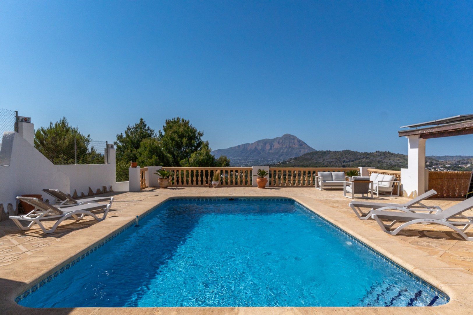 Piscina rectangular rodeada de una amplia terraza de piedra con balaustrada clásica y vistas directas al Montgó. Incluye zona de hamacas y mobiliario de descanso exterior.