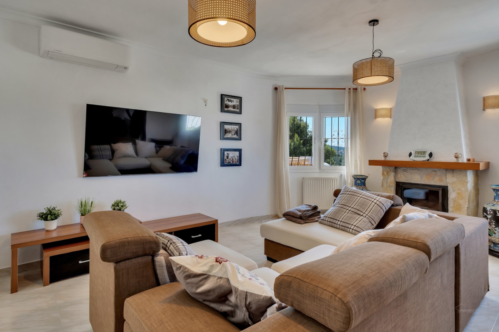 Salón luminoso con chimenea de piedra, aire acondicionado y amplios sofás. Incluye lámparas de mimbre, calefacción por radiadores y vistas a través de ventanas de doble acristalamiento.