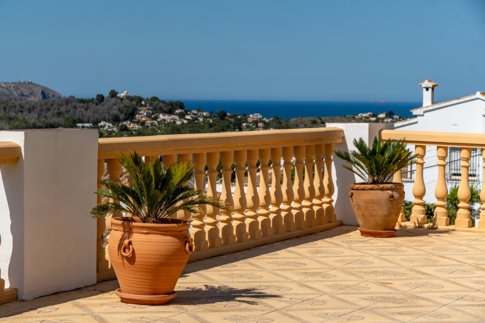 Terraza elevada con suelo cerámico decorado, balaustrada clásica y maceteros de terracota con vistas panorámicas al mar Mediterráneo y la costa de Jávea.