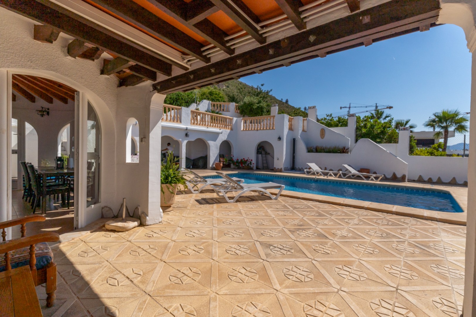 Terraza exterior con suelos cerámicos decorados, piscina rectangular y porche cubierto con vigas de madera. La arquitectura mediterránea se abre hacia las vistas del Montgó.