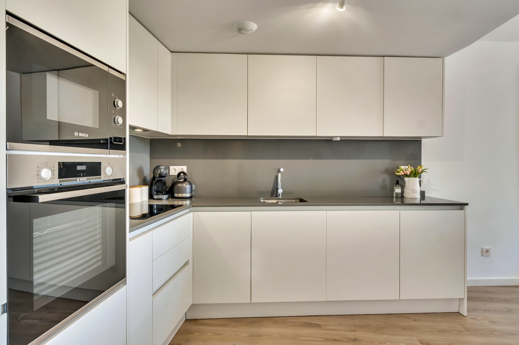 Cocina moderna de diseño minimalista con armarios blancos sin tiradores, encimera gris antracita y electrodomésticos Bosch integrados en columna.