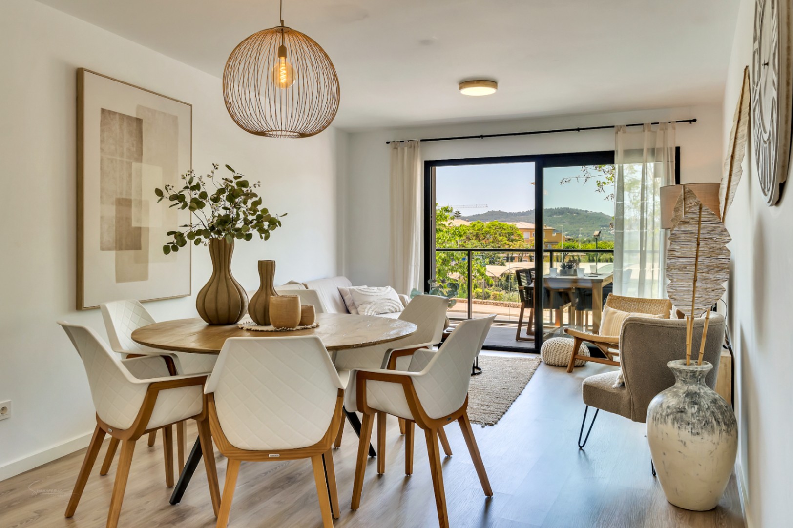 Comedor de concepto abierto con mesa circular de madera, sillas de diseño y acceso directo a la terraza con vistas despejadas hacia el paisaje de Jávea.