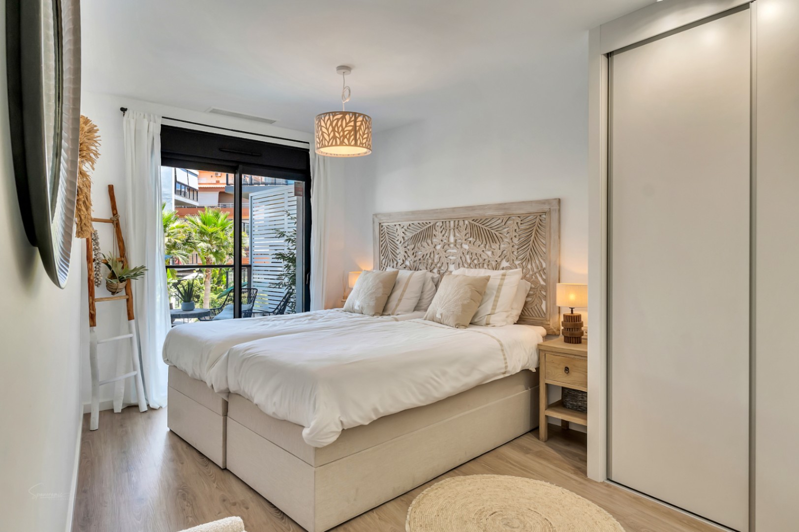 Dormitorio luminoso con cabecero de madera tallada, armario empotrado blanco y acceso directo a la terraza privada con vistas a la zona comunitaria.