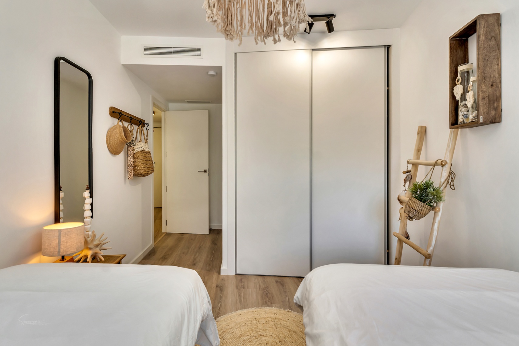 Dormitorio luminoso con dos camas, armario empotrado de puertas correderas, suelos de madera y decoración de estilo mediterráneo con fibras naturales.