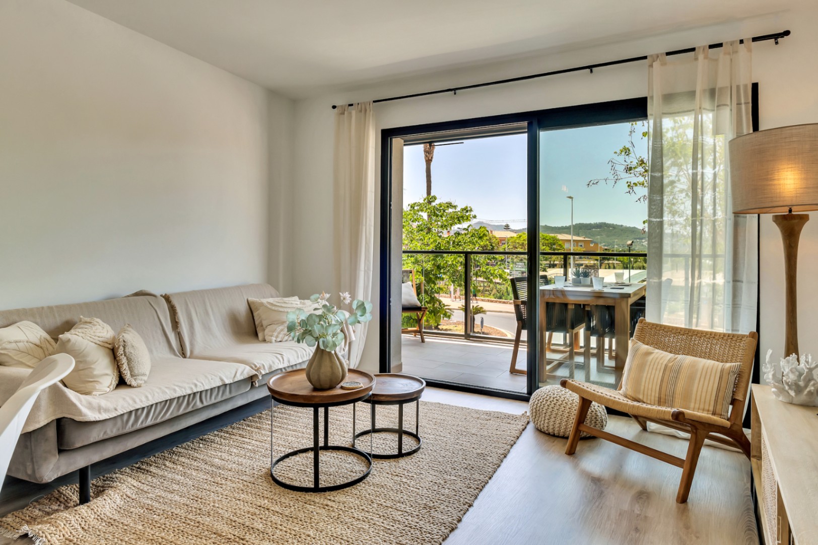 Salón luminoso con suelos de madera clara, mobiliario en tonos neutros y acceso directo a una terraza amueblada con vistas despejadas a través de amplios ventanales.