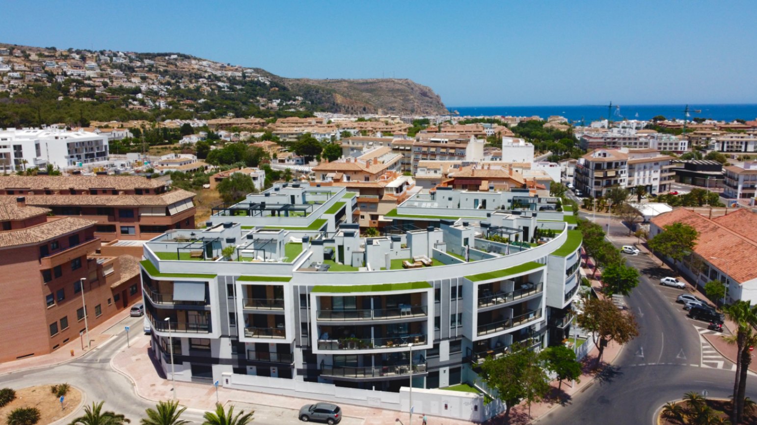 Vista aérea del complejo residencial moderno con arquitectura curva, destacando sus amplias terrazas privadas en la azotea y su proximidad al mar Mediterráneo en Jávea.