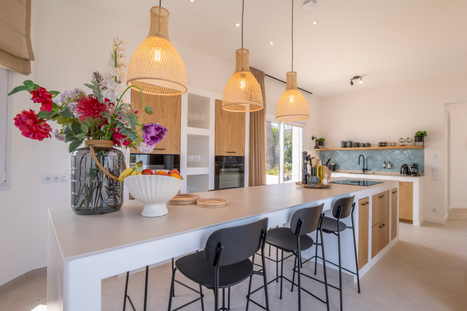Cocina moderna con isla central, taburetes negros y lámparas colgantes de mimbre.