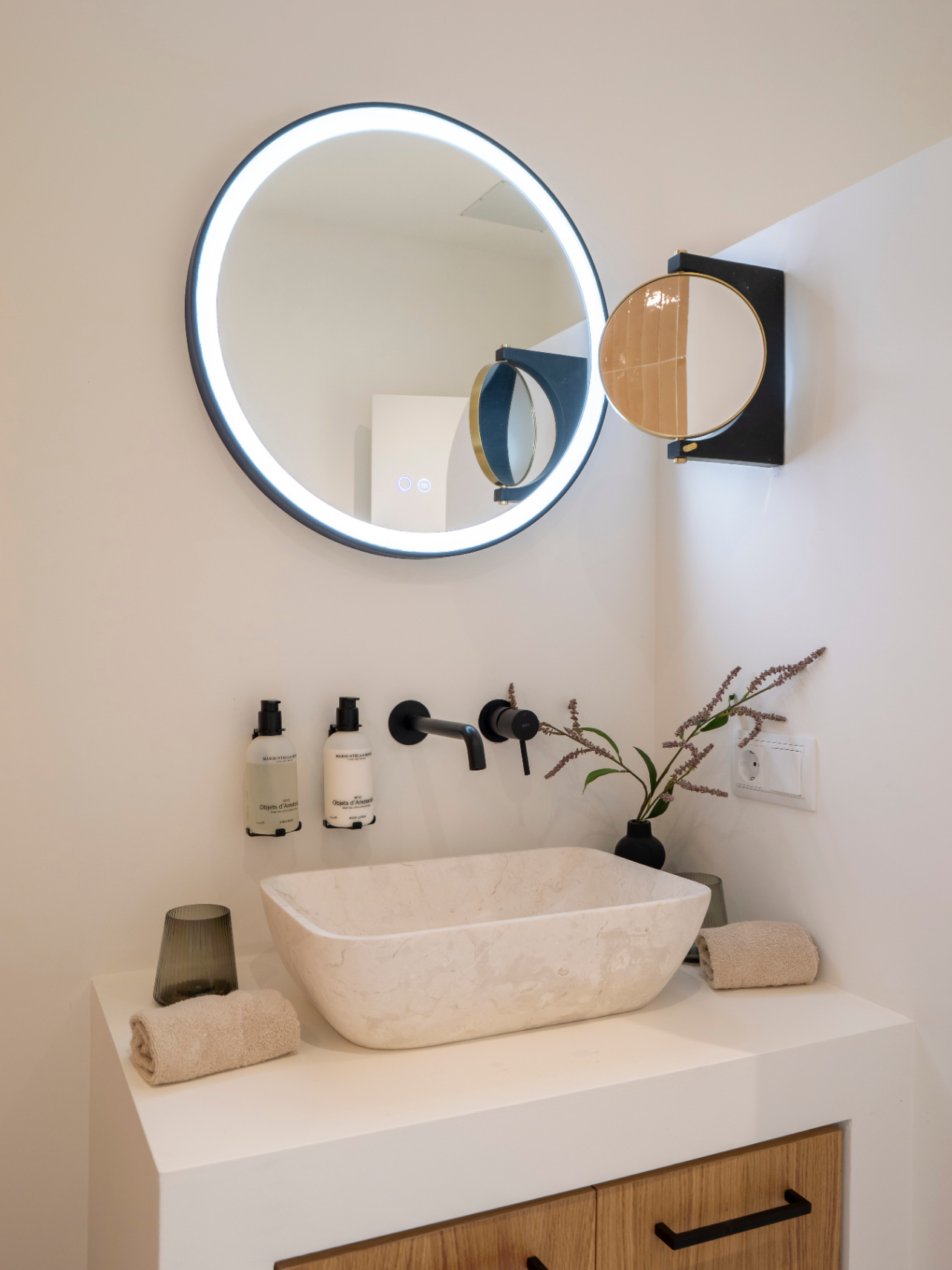 Detalle de baño con lavabo de piedra, grifería negra mate y espejo con iluminación LED.