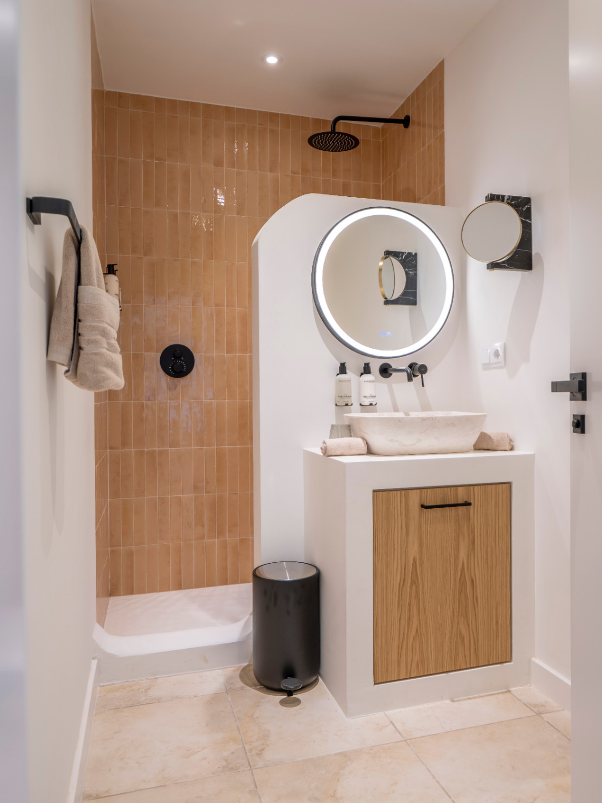 Detalle de baño moderno con ducha de obra y lavabo de piedra sobre mueble de madera clara.