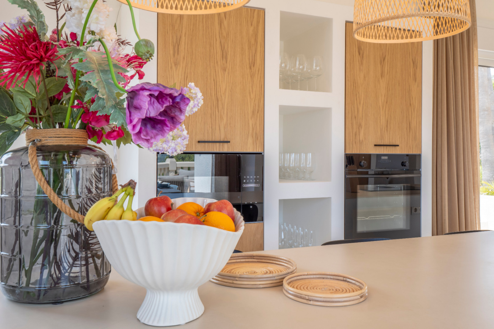 Detalle de la cocina con isla, armarios de madera clara y electrodomésticos negros.