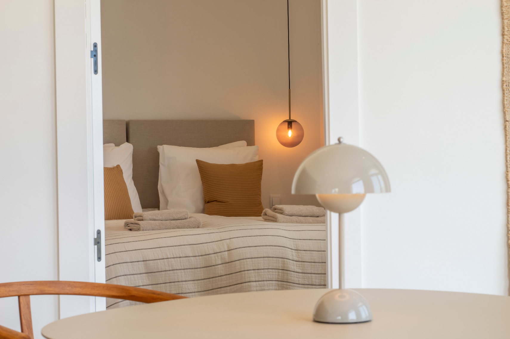 Dormitorio con cama doble, lámpara colgante esférica y ropa de cama a rayas. Mesa redonda con lámpara de noche.