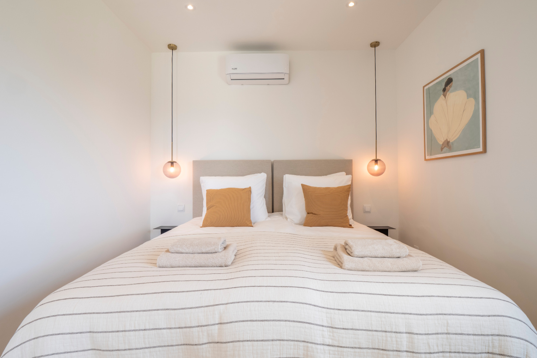 Dormitorio con cama doble, ropa de cama a rayas y lámparas colgantes esféricas.