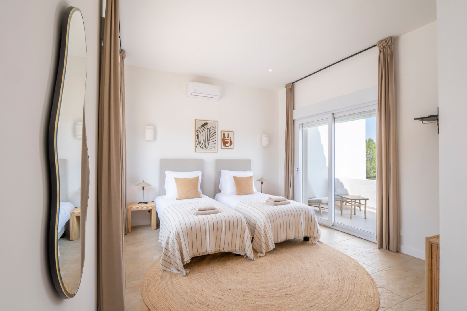 Dormitorio luminoso con dos camas individuales, alfombra redonda de yute y acceso a terraza exterior.
