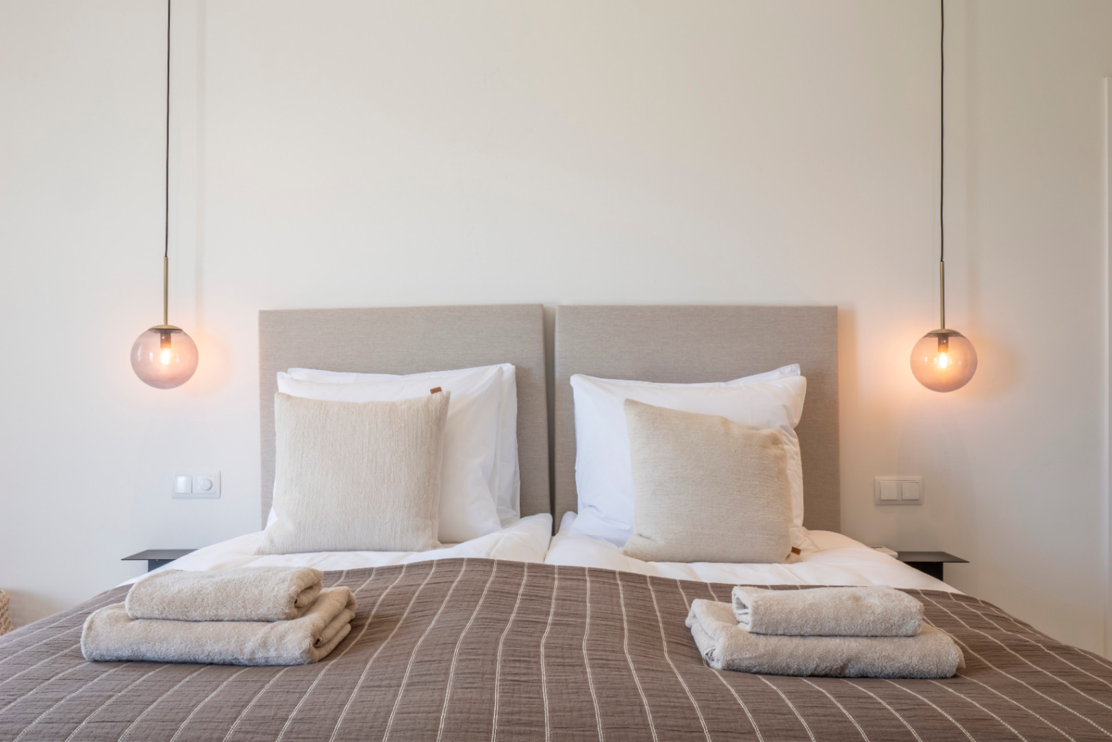 Habitación con dos camas individuales, cabeceros tapizados y lámparas colgantes de cristal color ámbar.