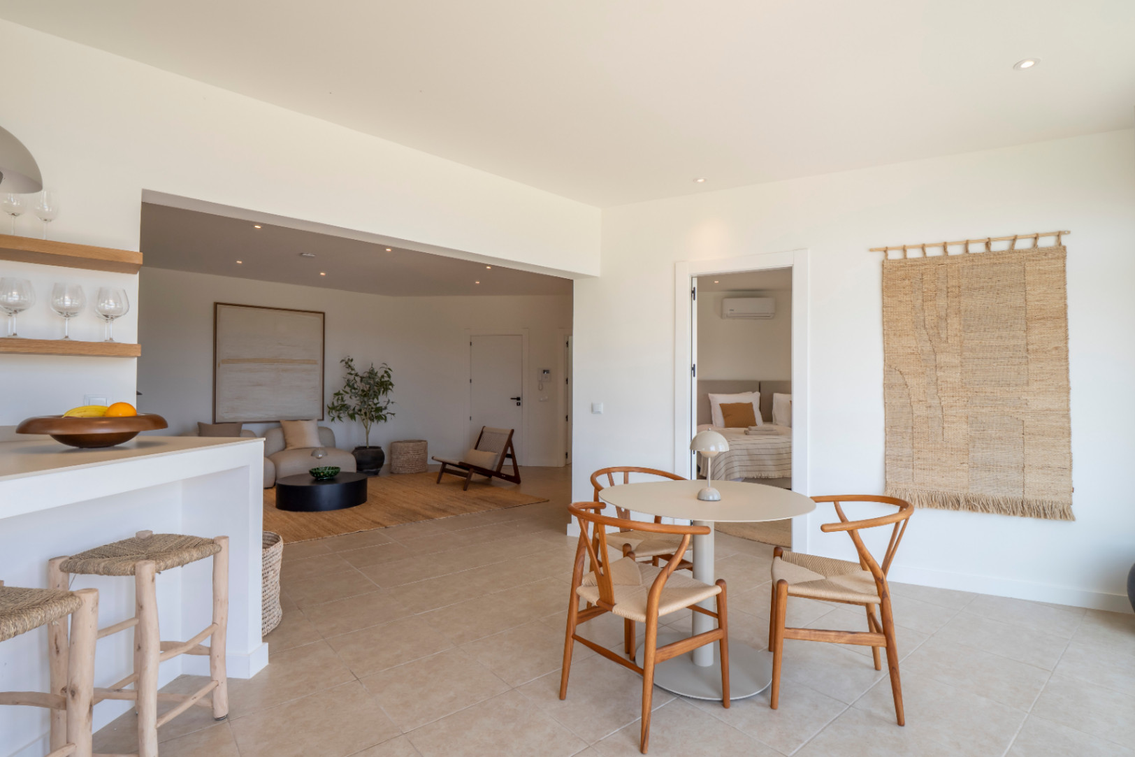 Interiores luminosos con mesa de comedor redonda y sillas de madera clara, integrados en un espacio diáfano con salón y cocina.
