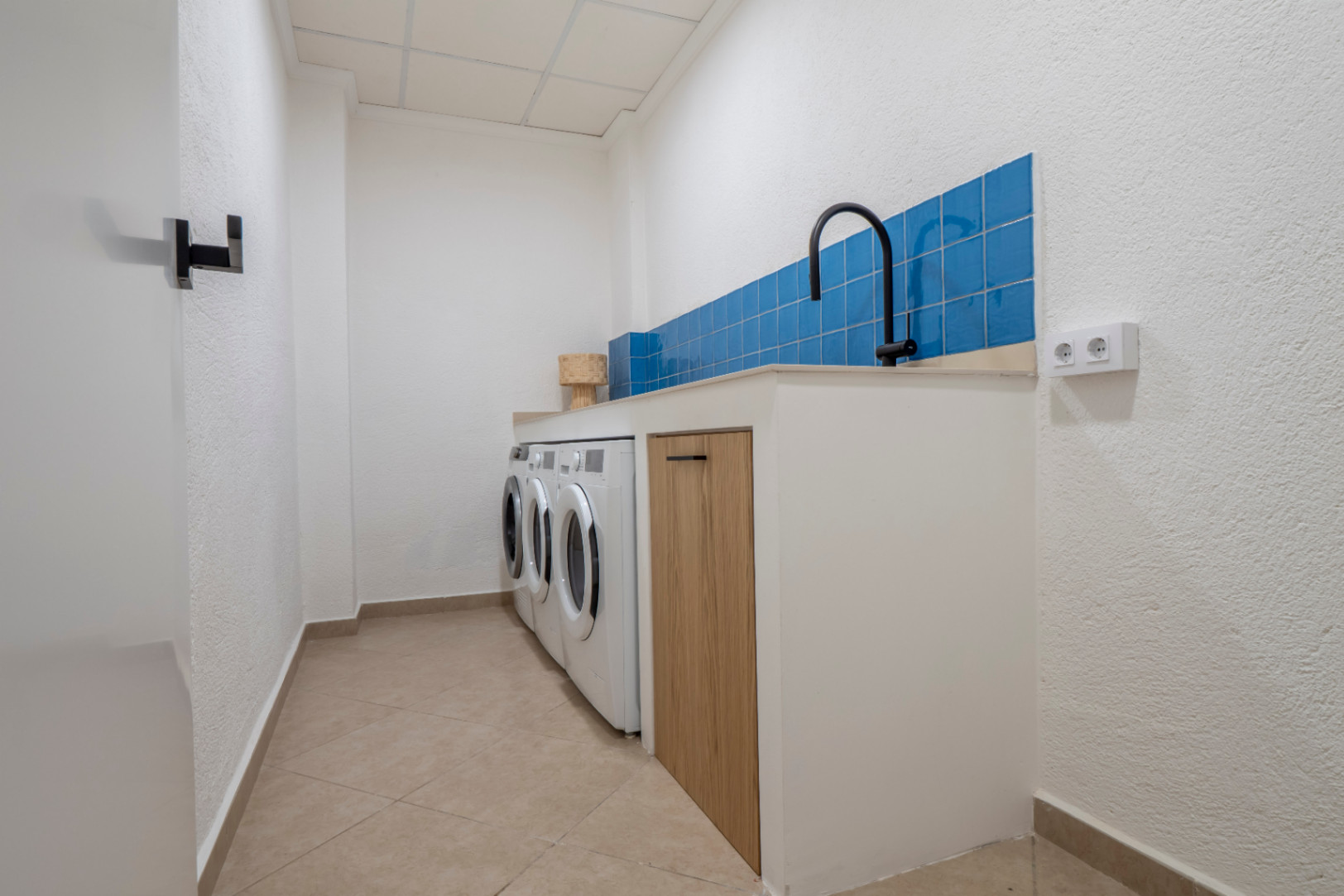 Lavadero funcional con azulejos azules, lavadoras y encimera de madera clara.