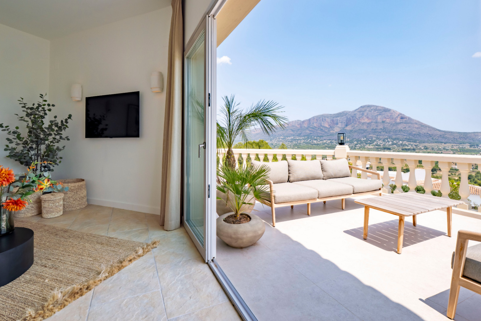 Terraza con vistas a la montaña, amueblada con sofá y mesa de centro de madera clara.