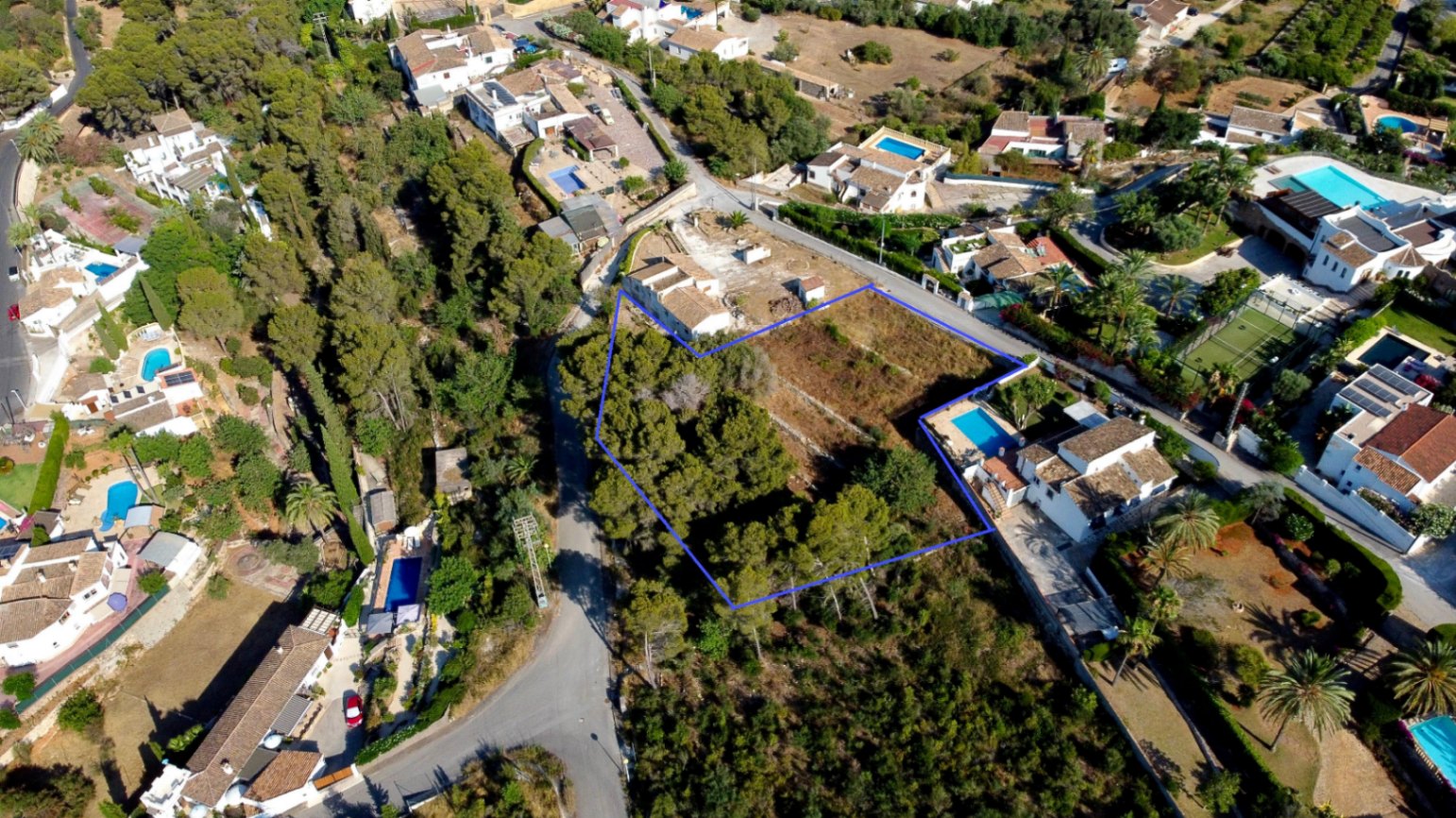 Vista aérea de la parcela urbana de 1.908 m² delimitada en azul, destacando su zona arbolada con pinos y su ubicación en una zona residencial consolidada de Jávea.