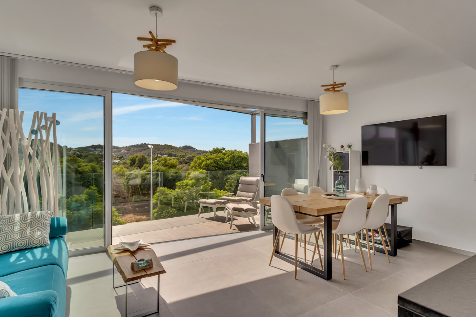 Salón comedor luminoso con grandes ventanales correderos que dan acceso a un balcón con vistas despejadas al entorno natural y mobiliario de diseño moderno.