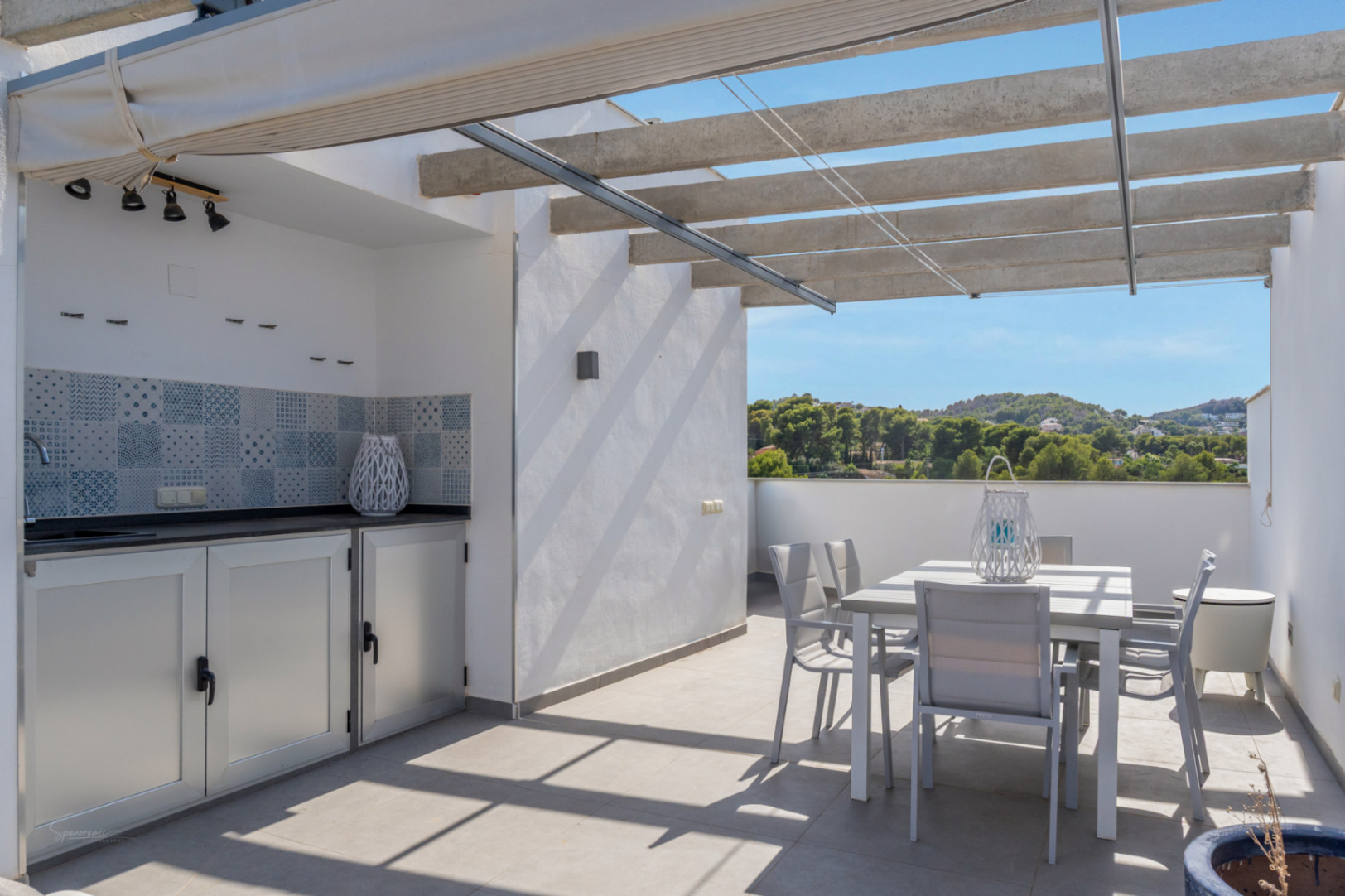 Terraza privada en la azotea con cocina de verano equipada, zona de comedor exterior y pérgola con toldo retráctil, ofreciendo vistas despejadas al entorno natural.