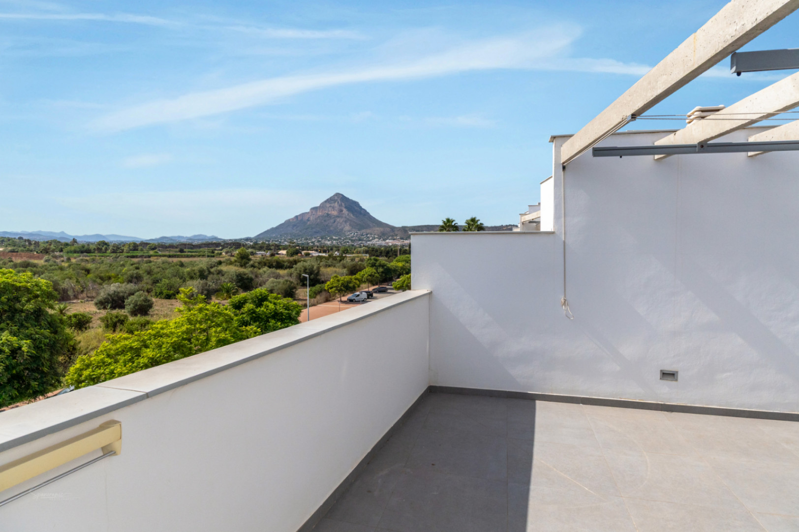 Terraza privada en la azotea con suelo de gres gris y vistas despejadas al Montgó y campos de cultivo, equipada con estructura de pérgola y muros minimalistas.