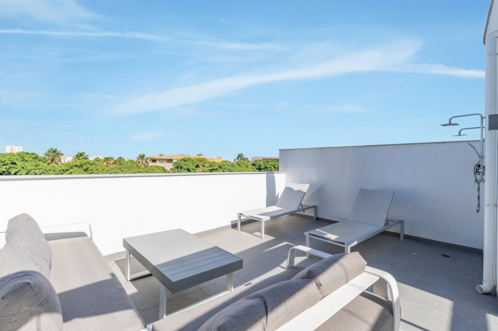 Terraza privada en la azotea equipada con zona de estar, tumbonas y ducha exterior. El espacio ofrece vistas despejadas a la vegetación circundante.