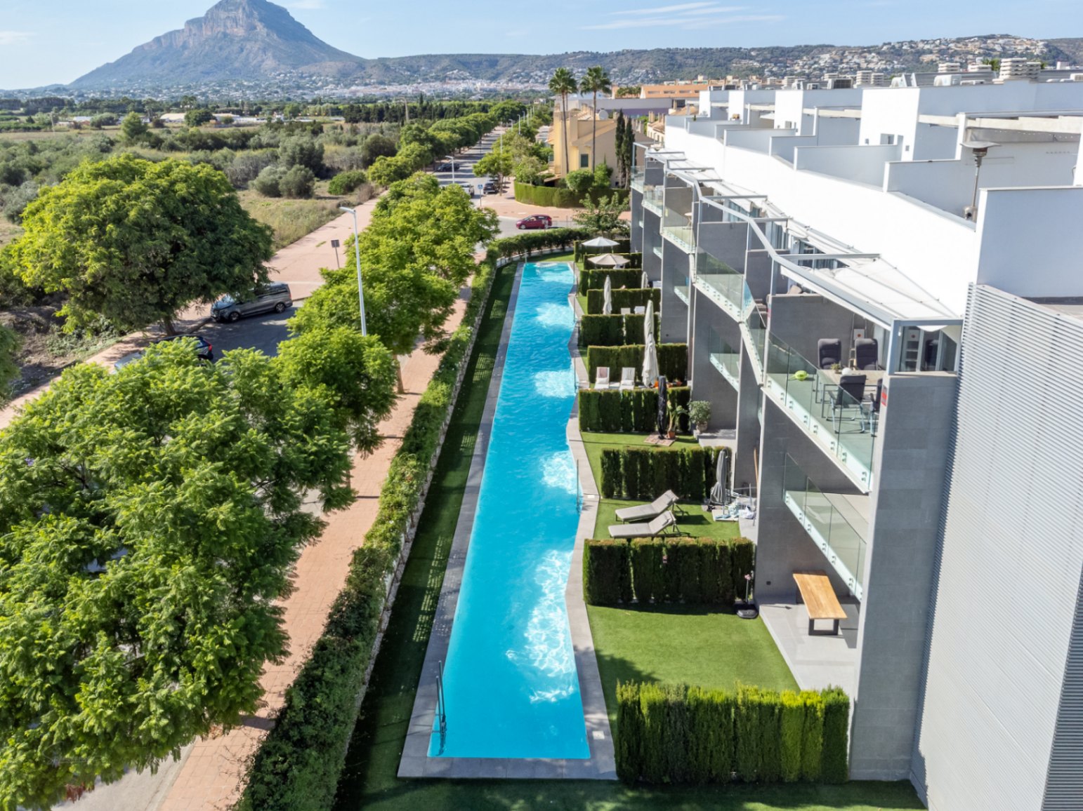 Vista aérea de la piscina comunitaria de 53 metros de largo, integrada en un entorno moderno con jardines privados y vistas despejadas a la montaña.