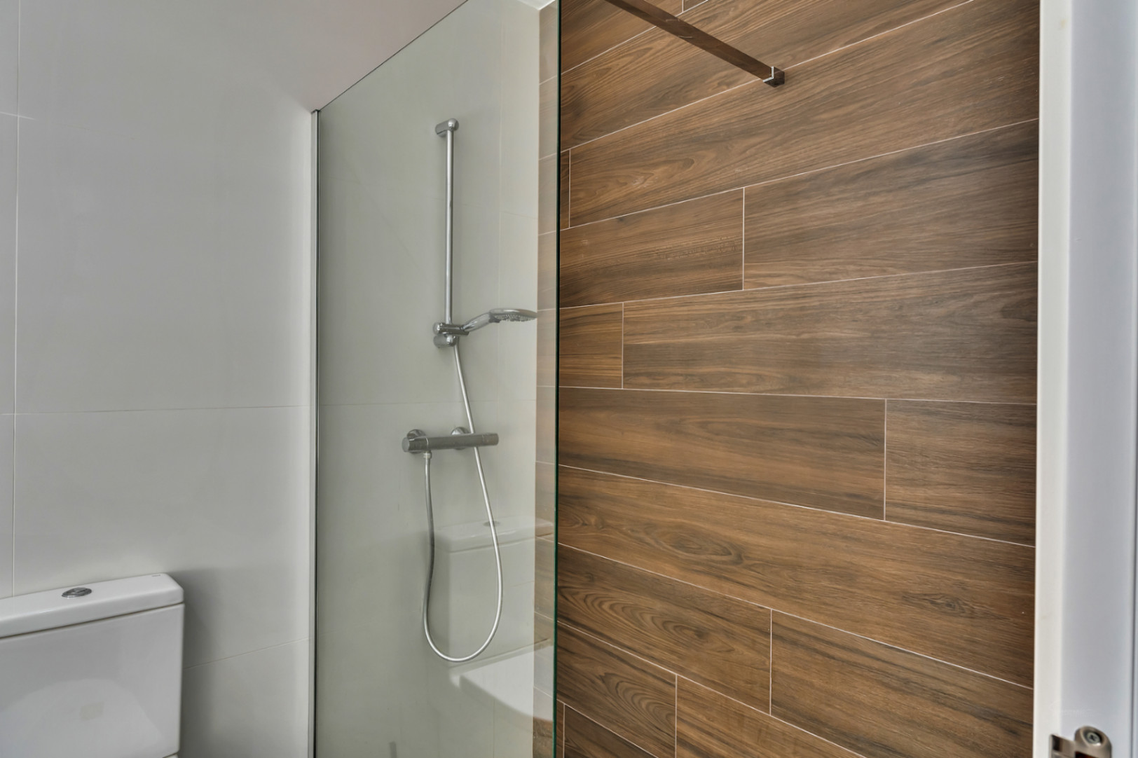 Baño moderno con ducha a ras de suelo, mampara de cristal fija y revestimiento cerámico con efecto madera que aporta calidez visual.