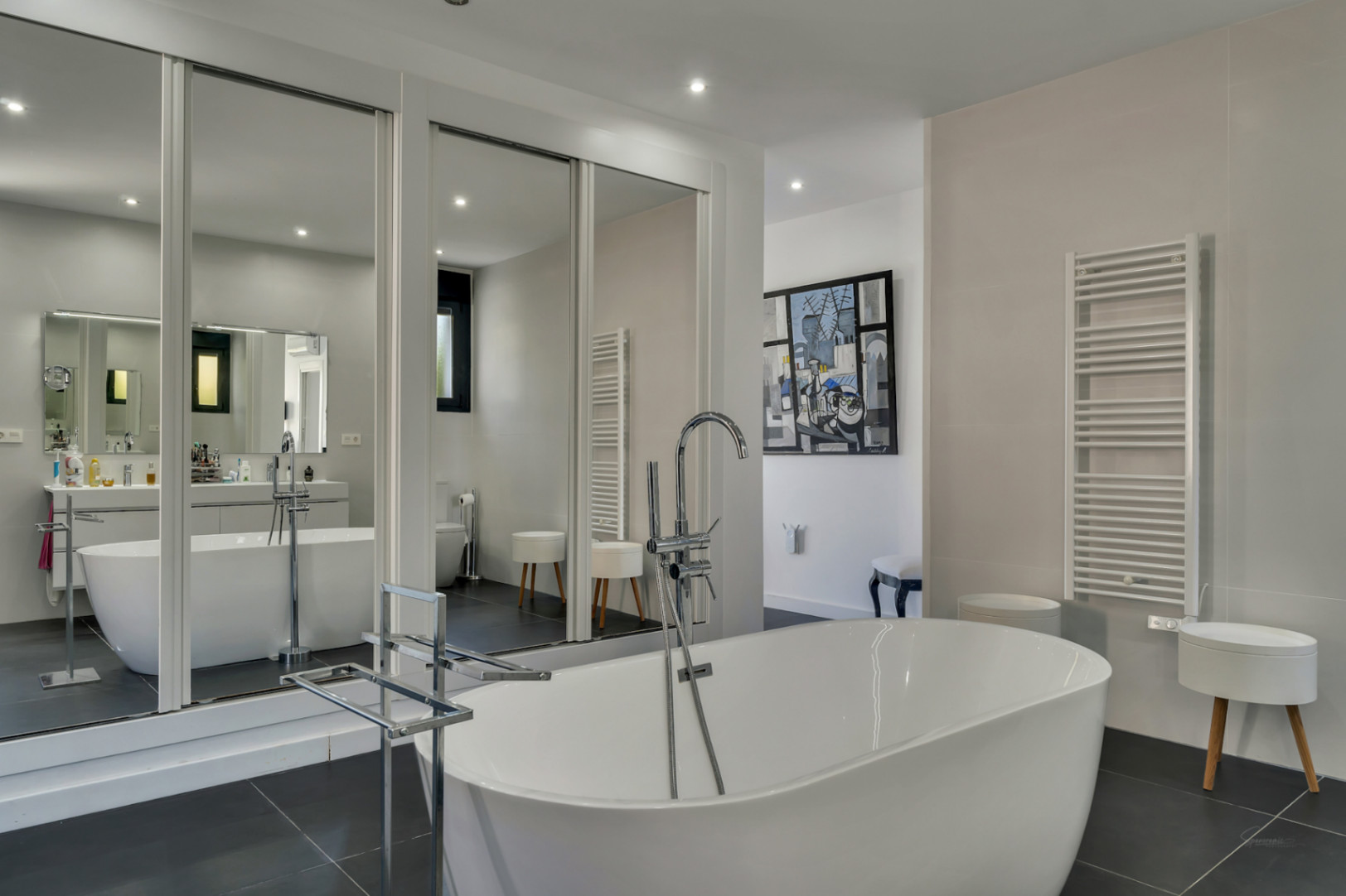 Baño principal con bañera exenta de diseño, grifería de pie cromada y amplios espejos de suelo a techo que aportan profundidad y luminosidad al espacio.