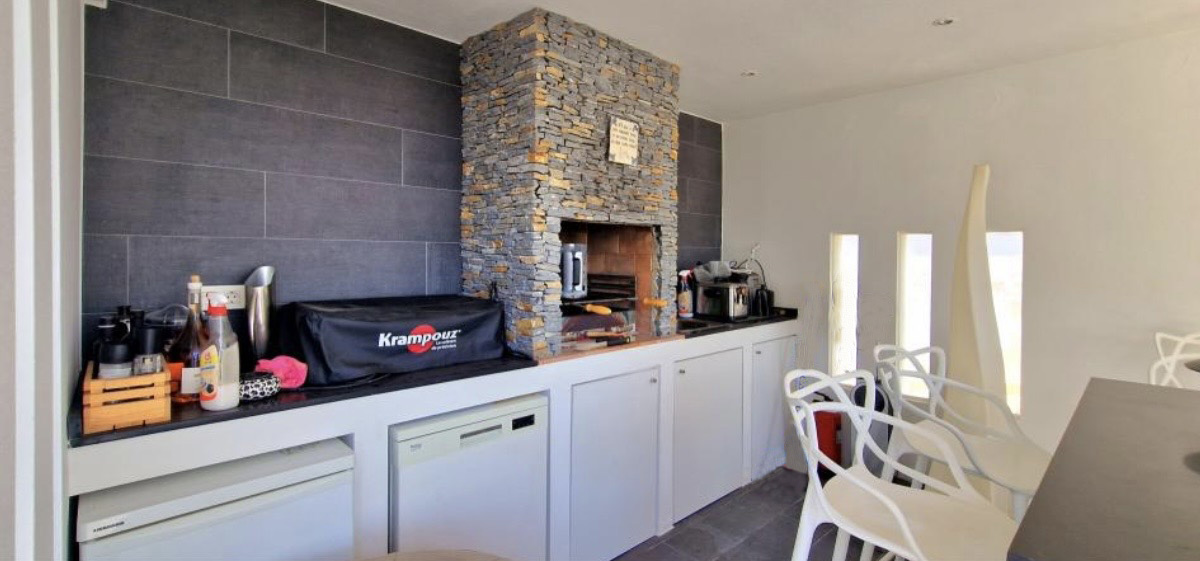 Cocina de verano equipada con barbacoa de piedra natural, encimera negra y electrodomésticos integrados bajo muebles blancos minimalistas.