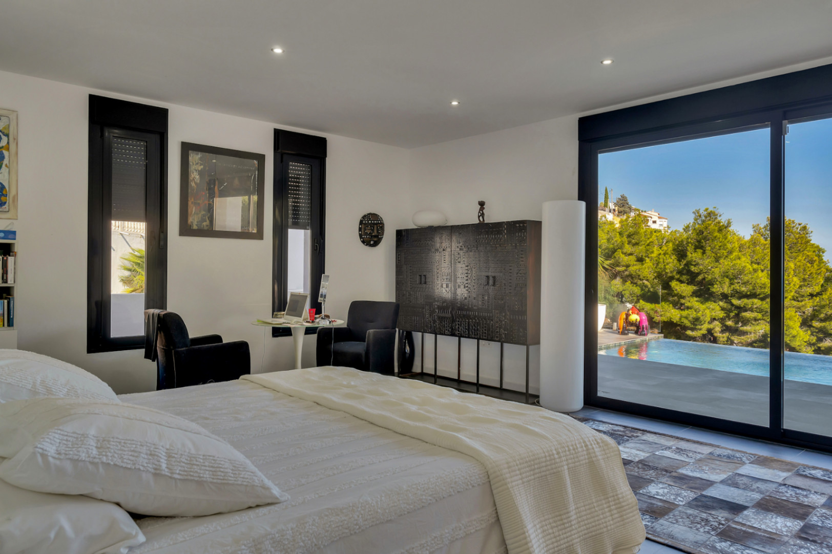 Dormitorio con acceso directo a la piscina mediante ventanales de carpintería negra, mobiliario de diseño oscuro y vistas despejadas al entorno natural.