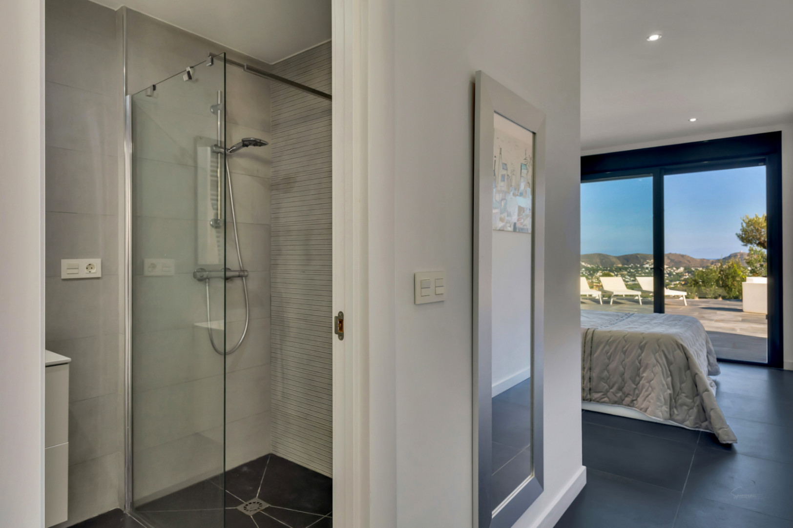 Dormitorio en suite con baño integrado que incluye ducha de obra acristalada. Al fondo, acceso directo a la terraza con vistas despejadas a la montaña.